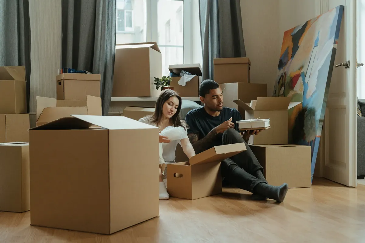 Couple unpacking cardboard boxes in a new apartment, surrounded by moving supplies.